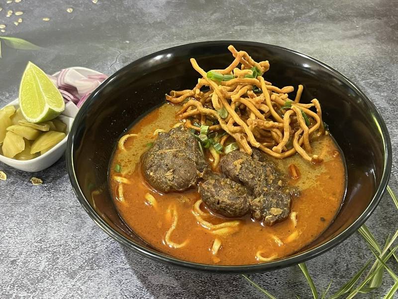 ข้าวซอยในชามดำ โรยเส้นกรอบ วางคู่ผักกาดดอง หอมแดง และมะนาว